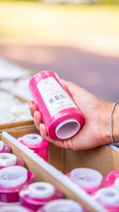 Hand hält pinke Nähgarnrolle über Garnkiste